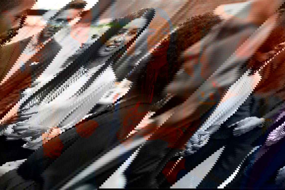 A business team is talking in the office. Image focuses on woman in the middle talking to a female colleague.